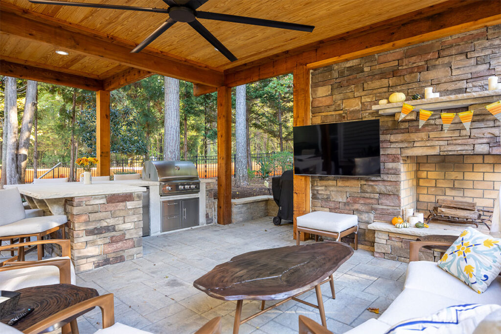 Interior shot underneath Trenton Woods pavilion show gathering area with couch, outdoor kitchen and television.