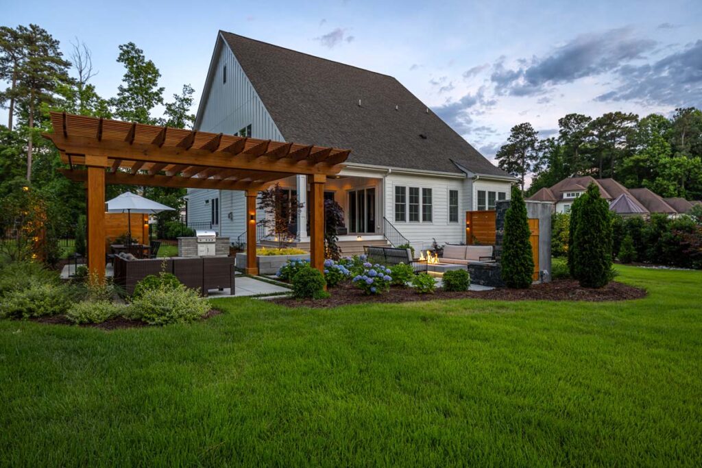 A view from backyard, showcasing Clear Falls pergola, patio furniture, and surrounding garden.