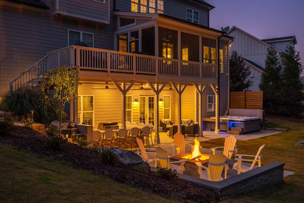 Three-quarter view of Roseroot patio facing composite deck, showcasing patio area with fire pit and deck with with out door kitchen underneath.