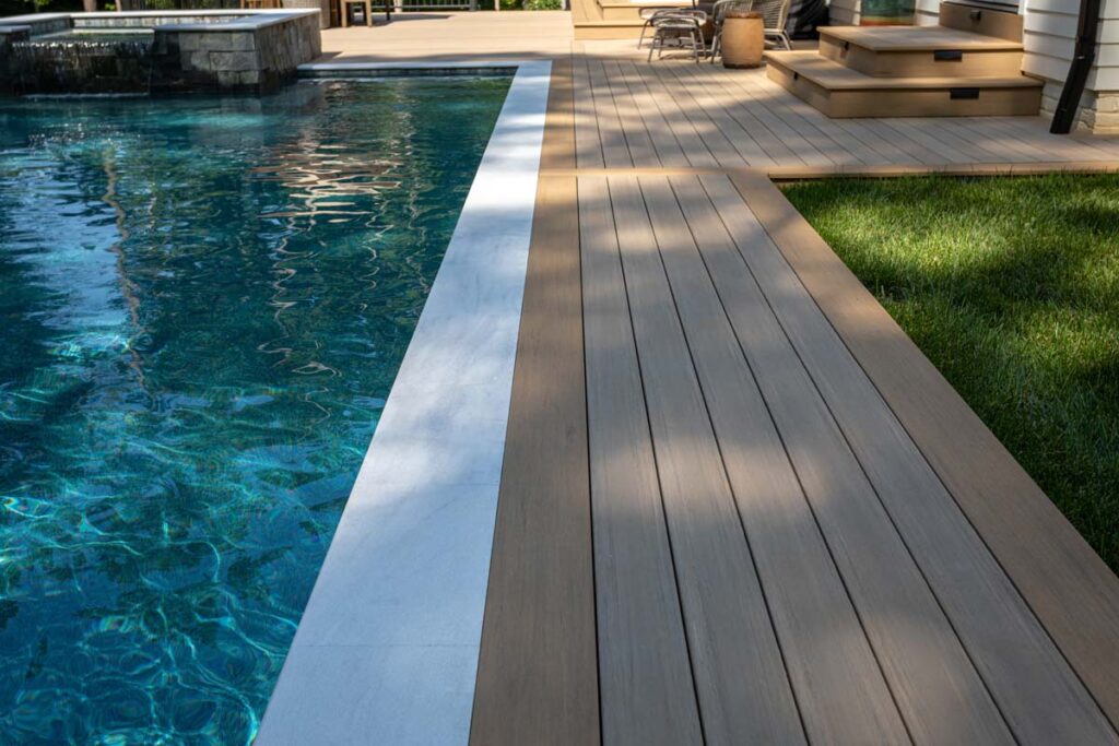 Close up of Royal Amber pool surrounds showing TimberTech composite deck, with patio in the background.