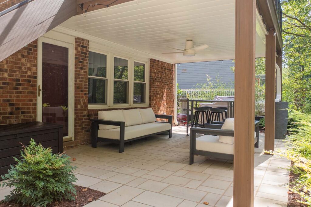 Close up of Rushing Brook deck, with two outdoor sofas, shrubs and storage box. Featuring patio door and stairs leading to the elevated deck.