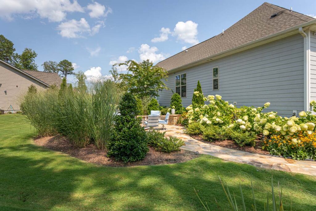 Three-quarter shot of Silver Dew patio with walkway leading to retaining wall with gathering area. Patio area is surrounded by landscape garden.