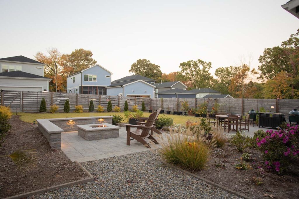 Wide shot of Steven patio project featuring, Techo-bloc pavers and fire pit. Revealing more of the neighborhood with wooden fence surrounding the property.