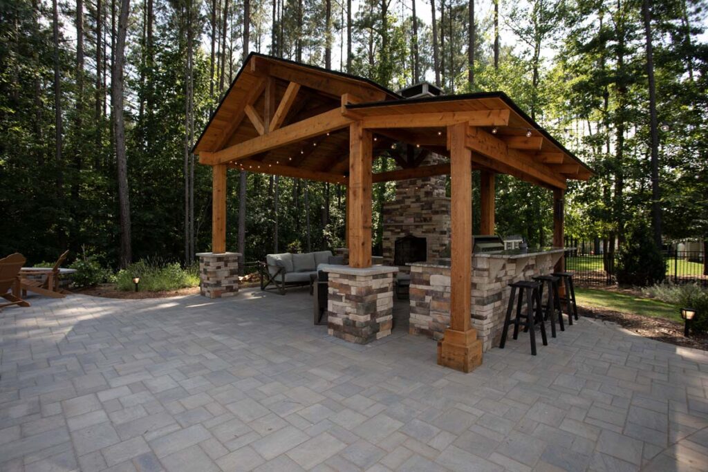 Wide shot of Swann Trail project showing custom built pavilion, with built-in, fireplace, outdoor kitchen and grill. Focusing on the counter top with three stools.