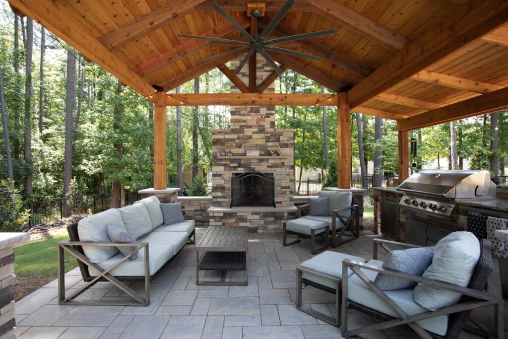 Wide shot of Swann Trail pavilion, showing fireplace, coffee table, outdoor kitchen, outdoor couch, and two chair.