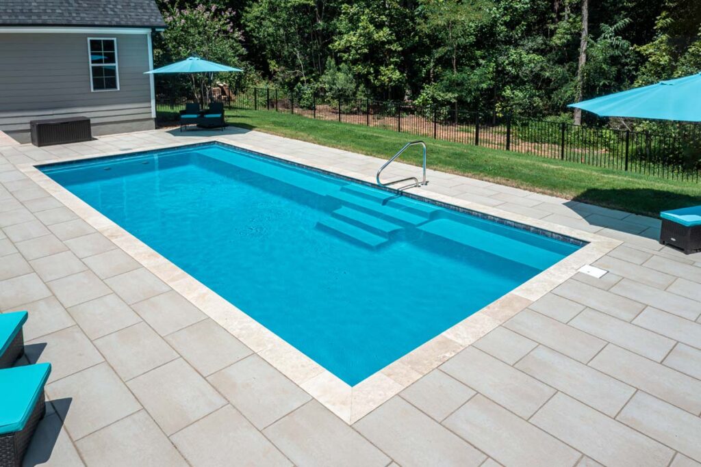 Wide shot view of Vision custom pool with Techo-Bloc patio pavers, with fire pit and patio in the background.