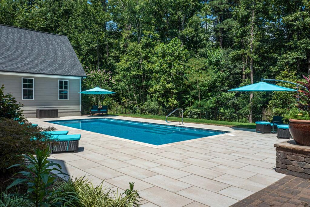 Wide shot view of Vision custom pool with Techo-Bloc patio pavers, with shrubs in the foreground.