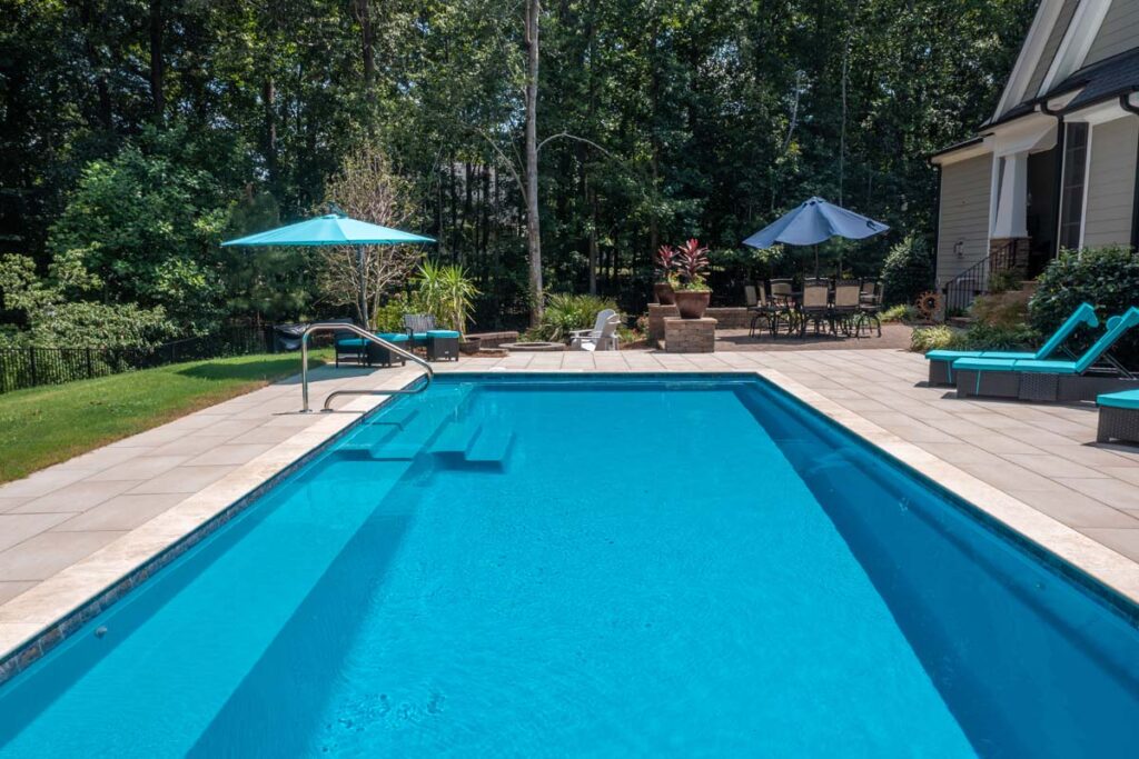 Wide shot view of Vision custom pool with Techo-Bloc patio pavers, with fire pit and patio in the background.