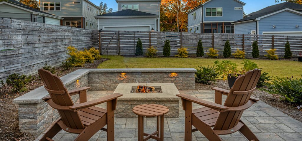 Front view of Stevens fire pit with two patio chairs surrounding fire pit. Patio paver features Techo-Bloc Eva Slate.