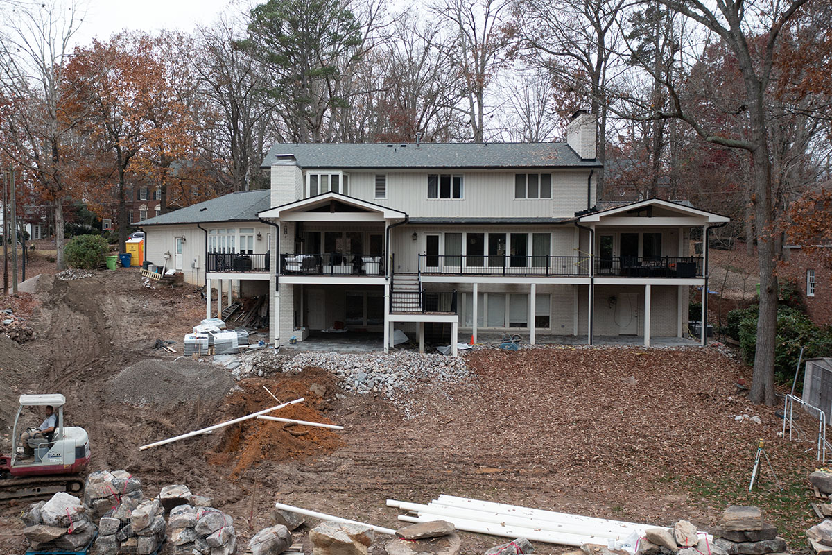 A wide-angle shot Sussex backyard showing a heavy machinery on the left side, with land being prepared to be graded and ground uncovering drainage system.